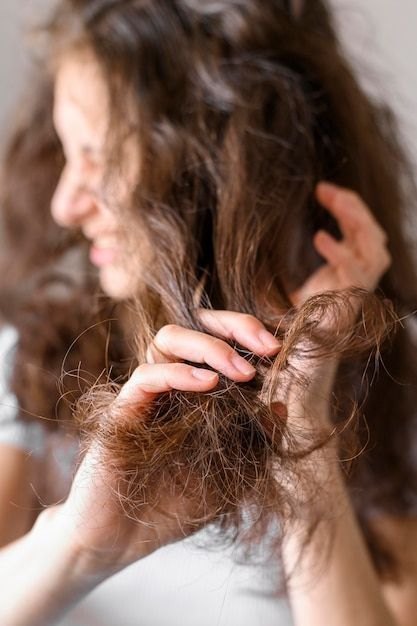 Phụ nữ cầm phần đuôi tóc khô xơ rối bằng hai tay trên nền trắng